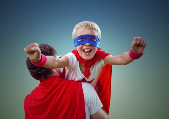 Man carrying kid in superhero costume Criança com fantasia de super herói apoiada no ombro do pai faz movimento de voar